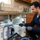 فني محترف يقوم بعملية تركيب فلاتر مياه منزلية بنظام 7 مراحل تحت حوض المطبخ باستخدام أدوات متخصصة.