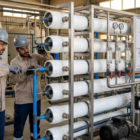 فنيان يربطان الأنابيب والوصلات بدقة خلال تركيب وحدات التناضح العكسي لمحطة التحلية.